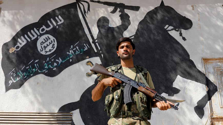 A member of Turkish-backed Free Syrian Army (FSA), seen with a mural of the Islamic State in the background, stands guard in front of a building in the border town of Jarablus, Syria, August 31, 2016. REUTERS/Umit Bektas TPX IMAGES OF THE DAY      - RTX2NQ4X