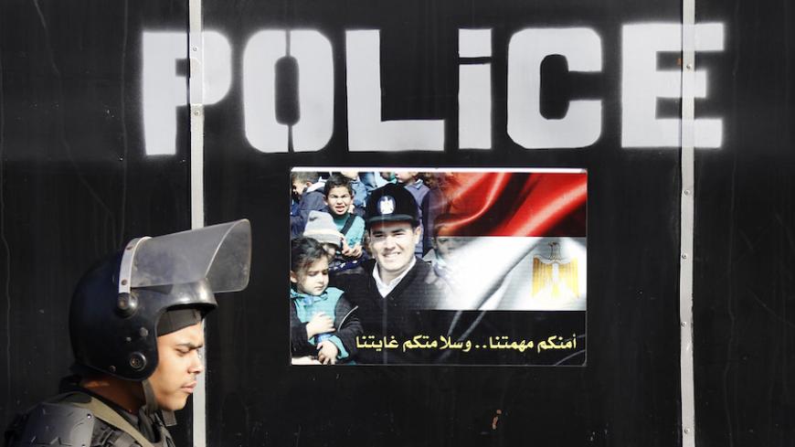 A riot police takes his position in front of a poster reading, "Our mission is your security and your safety our goal" outside a police academy, where ousted Egyptian President Mohamed Mursi's second trial session was due to take place, on the outskirts of Cairo January 8, 2014. The trial of Mursi on charges of inciting murder was postponed until February 1 on Wednesday after officials said bad weather had stopped him from being flown to court. REUTERS/Amr Abdallah Dalsh  (EGYPT - Tags: POLITICS CIVIL UNRES