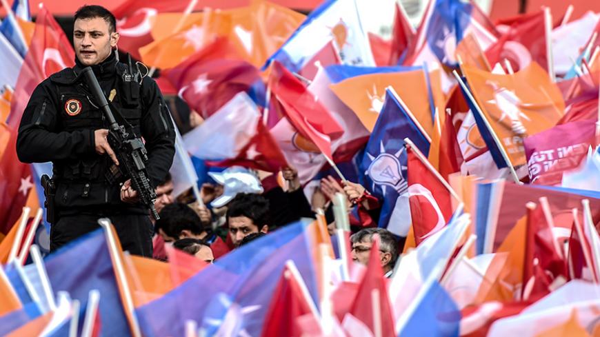A security stand guard while supporters wawe Turkish national and AKP party flags during a mass campaign rally of ruling Justice and Development Party (AKP) on October 25, 2015 at Yenikapi in Istanbul, a week ahead of the country's general elections on November 1.  AFP PHOTO/OZAN KOSE        (Photo credit should read OZAN KOSE/AFP/Getty Images)