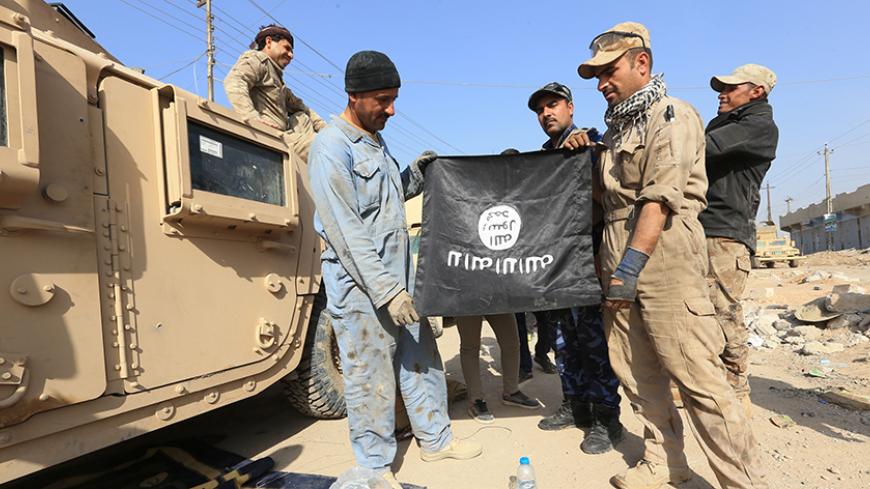 Iraqi soldiers pose with the Islamic State flag along a street in the Intisar district of eastern Mosul, Iraq, November 14, 2016, after capturing the same area from this district from the Islamic State on November 3. REUTERS/Air Jalal  - RTX2TL72
