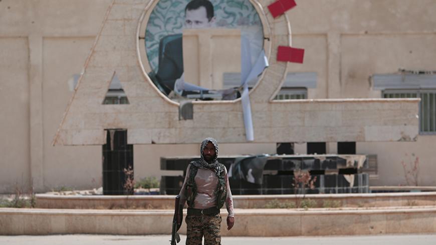 A Kurdish fighter from the People's Protection Units (YPG) carries his weapon as he walks at the faculty of economics where a defaced picture of Syrian President Bashar al-Assad is seen in the background, in the Ghwairan neighborhood of Hasaka, Syria, August 22, 2016. REUTERS/Rodi Said - RTX2MKNT