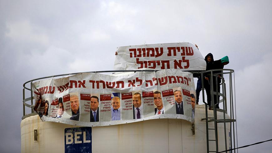 Israeli youths stand atop a water tank and attach banners in Hebrew reading "Amona will not fall for the second time" and "The government will not survive the eviction of Amona", in the Jewish settler outpost of Amona in the West Bank December 15, 2016. REUTERS/Ronen Zvulun - RTX2V5JX