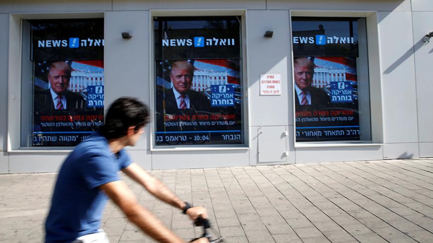 A man cycles past images of newly elected U.S. President Donald Trump which are displayed on monitors in Tel Aviv, Israel November 9, 2016. REUTERS/Baz Ratner - RTX2SSC2