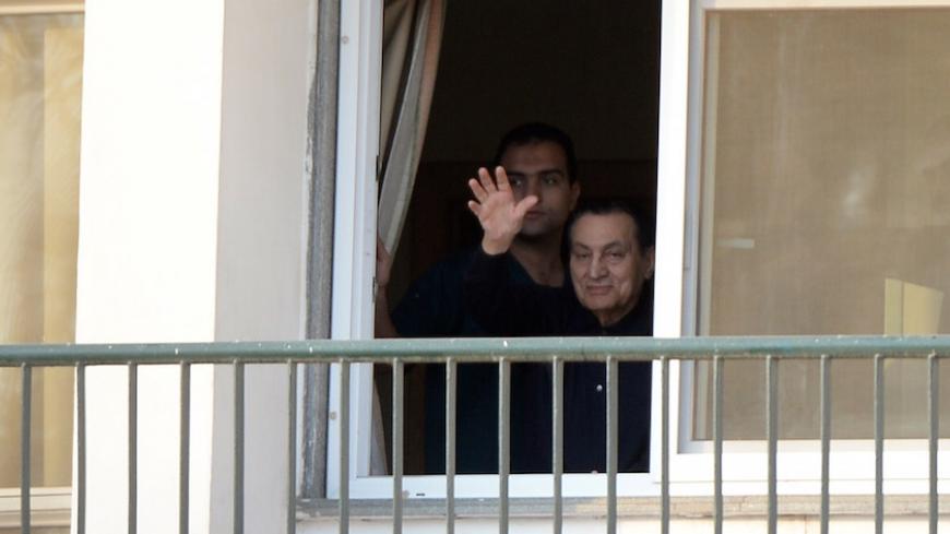 Egypt's former president Hosni Mubarak waves from his room at the Maadi military hospital in Cairo on May 4, 2015 as his supporters gather outside the building for his birthday. An Egyptian court is expected to examine on May 7, 2015 an appeal filed by the prosecution against a lower court's verdict that dropped murder charges against Mubarak and also acquitted six of his top security chiefs of charges of killing protesters during the 2011 uprising. Standing behind Mubarak is a doctor. AFP PHOTO / MOHAMED E