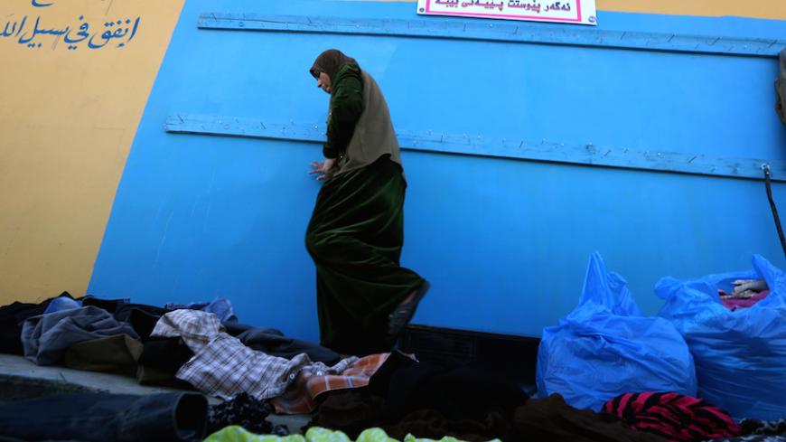 TOPSHOT - A woman walks amid a pile of clothes next to an outdoor charity wall marked as "the generous wall", an initiative encouraging people to donate clothes to those in need and open for people to collect items they need to keep warm, in Arbil, the capital of the autonomous Kurdish region of northern Iraq, on February 27, 2016. / AFP / SAFIN HAMED        (Photo credit should read SAFIN HAMED/AFP/Getty Images)
