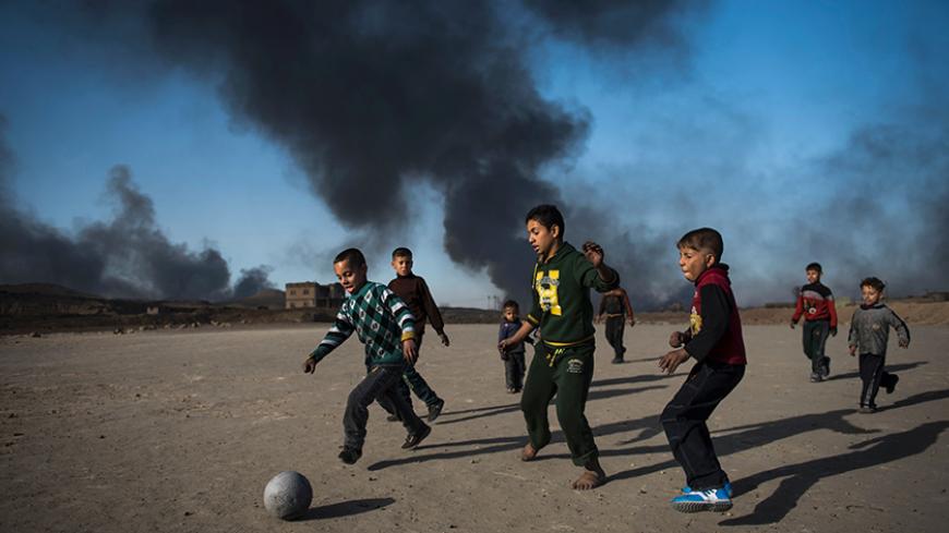 TOPSHOT - Children play football as oil wells, set ablaze by retreating Islamic State (IS) jihadists, burn behind them in the town of Qayyarah, some 70 km south of Mosul on November 20, 2016.
Locals told AFP that they face a range of health issues including breathing difficulties, and sheperds said they could not sell their livestock as the sheep's fleece was blackened by smoke. / AFP / Odd ANDERSEN        (Photo credit should read ODD ANDERSEN/AFP/Getty Images)