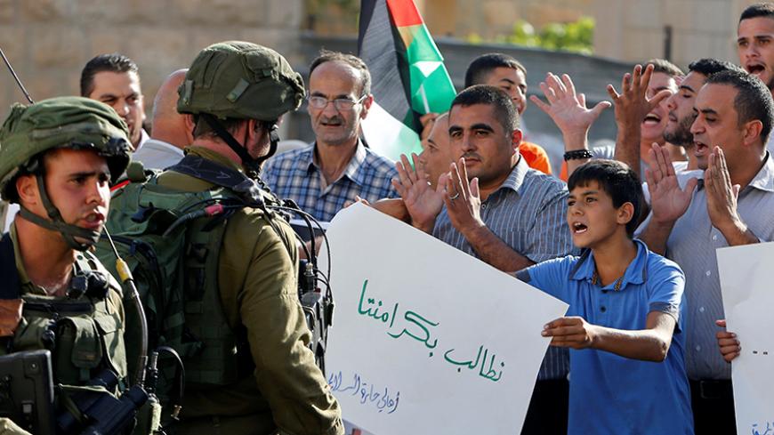 A Palestinian boy holds a sign that reads "we demand our dignity" in front of  Israeli soldiers during a protest calling for the reopening of a closed street in the West Bank city of Hebron August 24, 2016.  REUTERS/Mussa Qawasma  - RTX2MW1E