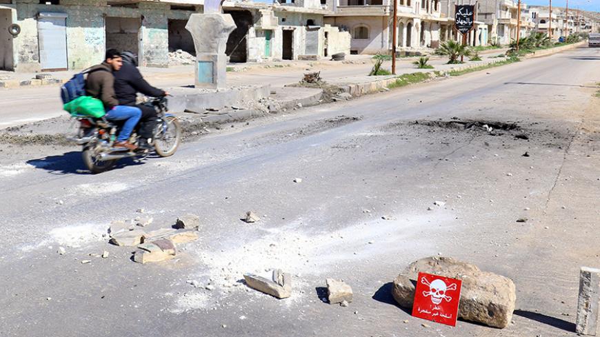 Men ride a motorbike past a hazard sign at a site hit by an airstrike on Tuesday in the town of Khan Sheikhoun in rebel-held Idlib, Syria April 5, 2017. The hazard sign reads, "Danger, unexploded ammunition". REUTERS/Ammar Abdullah - RTX3475J