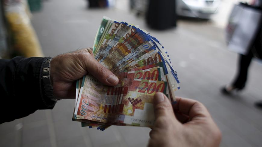 A Palestinian money exchanger displays money at a market in the West Bank city of Ramallah March 25, 2015. Israel's decision to withhold $130 million a month in revenue collected on behalf of the Palestinians is strangling the economy and leaving the banking system dangerously exposed, the Palestinian central bank governor said on Wednesday. REUTERS/Mohamad Torokman - RTR4UT7Y