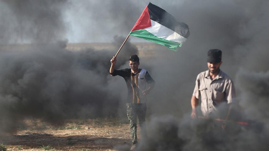 A protester holds a Palestinian flag during clashes with Israeli troops at a protest against reducing power supply to Gaza, near the border with Israel in Khan Younis in the southern Gaza Strip June 20, 2017. REUTERS/Ibraheem Abu Mustafa - RTS17WD5