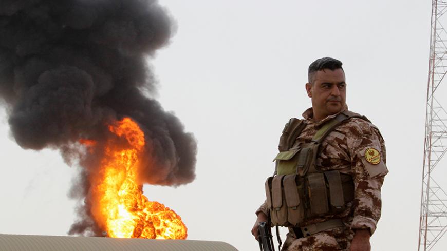 A member of the Kurdish Peshmerga forces stands guard as smoke rises after an attack at Bai Hassan oil station, northwest of Kirkuk, Iraq, July 31, 2016. REUTERS/Ako Rasheed - RTSKFGY