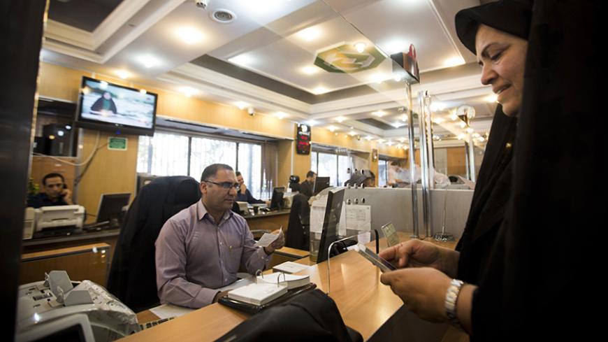 An Iranian woman uses a mobile phone as a bank clerk proceeds her request at the Export Development Bank of Iran in the capital Tehran on July 27, 2015. Iran's central bank chief said that Iran has assets of $29 billion in overseas banks that could be unlocked under a nuclear deal struck on July 14, far less than reported estimates of over $100 billion. AFP PHOTO / BEHROUZ MEHRI        (Photo credit should read BEHROUZ MEHRI/AFP/Getty Images)