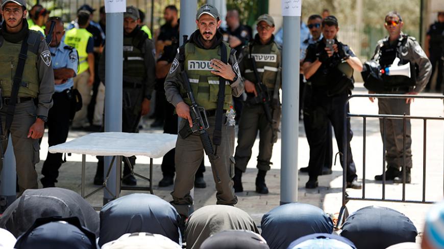 Palestinians pray as Israeli police officers look on by newly installed metal detectors at an entrance to the compound known to Muslims as Noble Sanctuary and to Jews as Temple Mount in Jerusalem's Old City July 16, 2017. REUTERS/Ronen Zvulun - RTX3BN0P