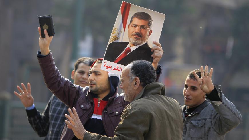 Supporters of the Muslim Brotherhood and ousted Egyptian President Mohamed Mursi hold a copy of the Koran and Mursi's picture at Talaat Harb Square, in Cairo, January 25, 2015. A bomb wounded two Egyptian policemen in Cairo on Sunday and security forces moved quickly to disperse small protests on the anniversary of the popular uprising that toppled autocrat Hosni Mubarak in 2011, officials said. REUTERS/Mohamed Abd El Ghany (EGYPT - Tags: POLITICS CIVIL UNREST) - RTR4MSGL