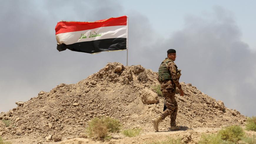 A soldier walks past an Iraqi flag in Husaybah, in Anbar province July 22, 2015. Iraqi security forces and Sunni tribal fighters launched an offensive on Tuesday to dislodge Islamic State militants and secure a supply route in Anbar province, police and tribal sources said. REUTERS/Stringer - GF10000167090