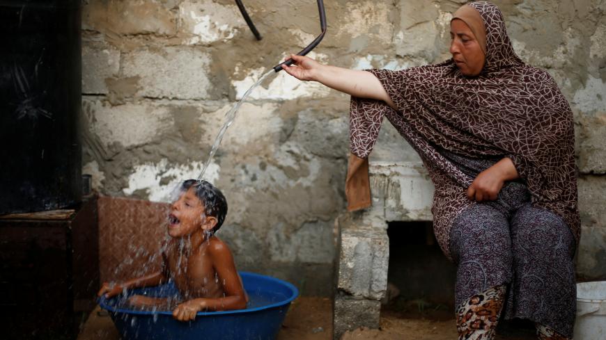 A Palestinian woman bathes her son with water from a tank, filled by a charity, inside their dwelling in Khan Younis, in the southern Gaza Strip, July 3, 2017. REUTERS/Mohammed Salem             SEARCH "GAZA HEAT" FOR THIS STORY. SEARCH "WIDER IMAGE" FOR ALL STORIES. - RC1FC4354260