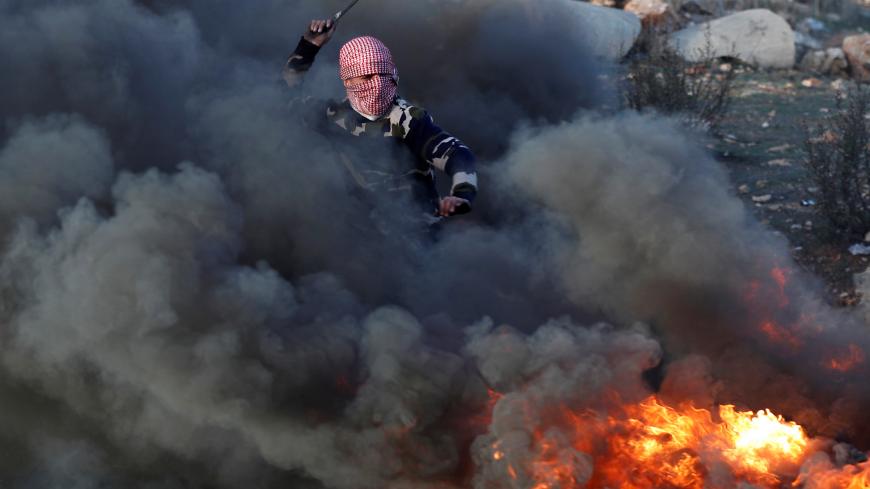 A masked Palestinian throws a stone at Israeli forces in front of a burned barricade during a protest against U.S. President Donald Trump's decision to recognize Jerusalem as the capital of Israel, near the Jewish settlement of Beit El, near the West Bank city of Ramallah December 11, 2017. REUTERS/Goran Tomasevic - RC1AAB56ECF0