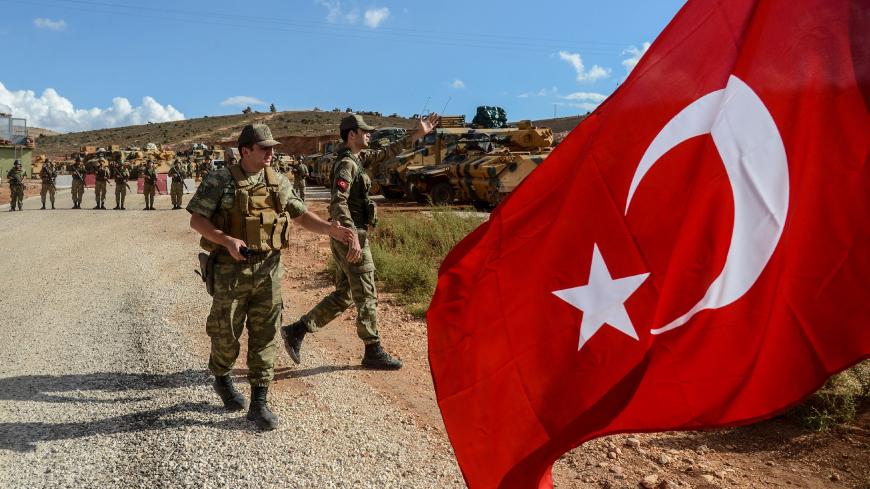 Turkish soldiers stand near armoured vehicles as a man waves a Turkish national flag during a demonstration in support of the Turkish army's Idlib operation near the Turkey-Syria border near Reyhanli, Hatay, on October 10, 2017.
The Turkish army has launched a reconnaissance mission in Syria's largely jihadist-controlled northwestern Idlib province in a bid to create a de-escalation zone, the military said on October 9.  / AFP PHOTO / ILYAS AKENGIN        (Photo credit should read ILYAS AKENGIN/AFP/Getty Im