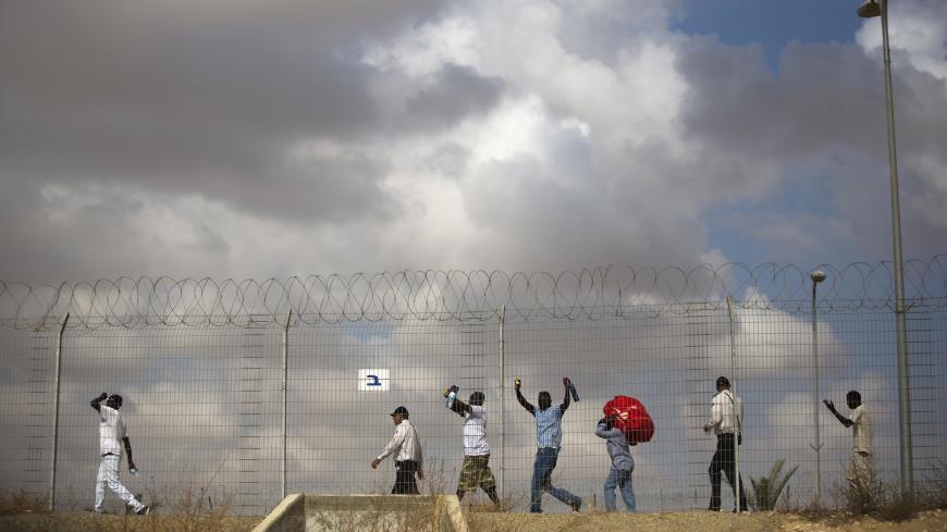 African migrants walk behind a fence as they leave Holot detention centre in Israel's southern Negev desert August 25, 2015. Israel on Tuesday began releasing some 1,200 African migrants whom it has interned for more than a year in the detention centre. Under the terms of their release, they are banned from living or working in Tel Aviv and the southern resort city of Eilat, which both have large migrant communities. Two weeks ago, Israelís Supreme Court reduced from 20 months to 12 months the period of tim