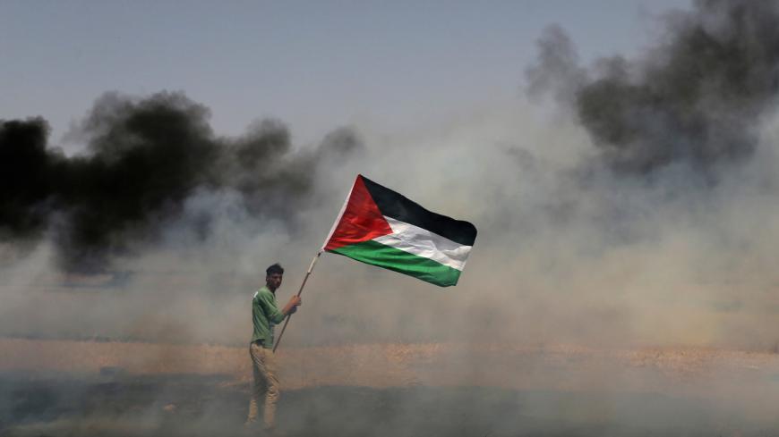 A demonstrator holds a Palestinian flag during clashes with Israeli troops at a protest where Palestinians demand the right to return to their homeland, at the Israel-Gaza border in the southern Gaza Strip, April 13, 2018. REUTERS/Ibraheem Abu Mustafa     TPX IMAGES OF THE DAY - RC151862B9A0