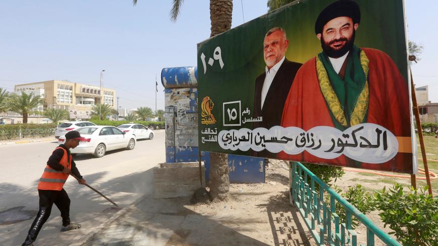 A worker cleans the street next to a campaign poster of candidates ahead of the parliamentary election, in Najaf, Iraq, April 14, 2018. REUTERS/Alaa Al-Marjani - RC155ACA6900
