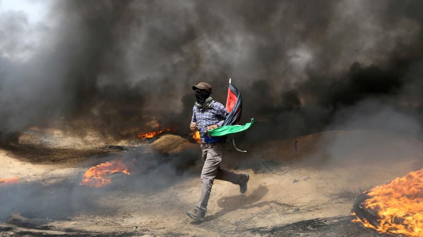 A demonstrator runs during clashes with Israeli troops at a protest where Palestinians demand the right to return to their homeland, at the Israel-Gaza border in the southern Gaza Strip, April 20, 2018. REUTERS/Ibraheem Abu Mustafa     TPX IMAGES OF THE DAY - RC1B7BFE3220