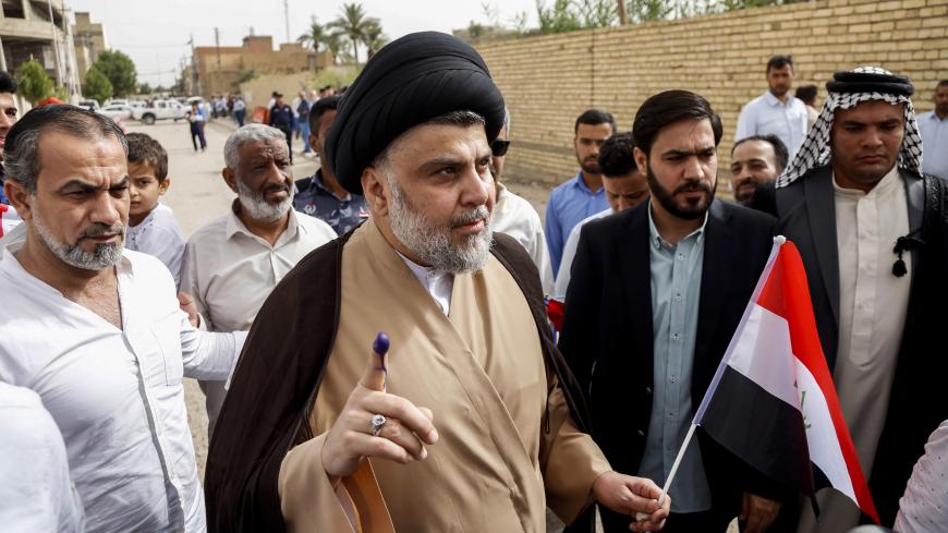Iraqi Shiite cleric and leader Moqtada al-Sadr (C-L) shows his ink-stained index finger and holds a national flag while surrounded by people outside a polling station in the central holy city of Najaf on May 12, 2018 as the country votes in the first parliamentary election since declaring victory over the Islamic State (IS) group. - Polling stations opened at 7:00 am for the roughly 24.5 million registered voters to cast their ballots across the conflict-scarred nation. (Photo by Haidar HAMDANI / AFP)      