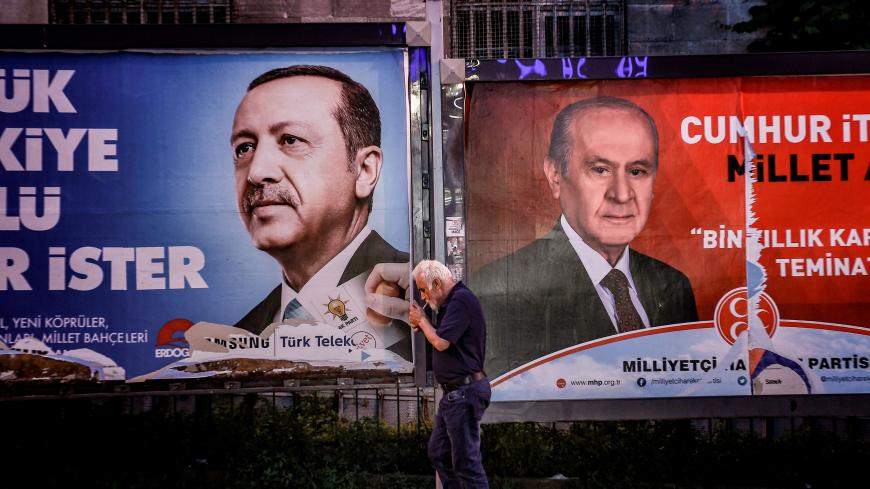 A pedestrian lights a cigarette as he walks past in banners with portraits of Turrkish President Recep Tayyip Erdogan (L) and the leader of Nationalist Movement Party (MHP) Devlet Bahceli in Istanbul on June 19, 2018. - Turkey is preparing for tight presidential and parliamentary elections on June 24, while many analysts say President Erdogan wants a major foreign policy success to give him a final boost. (Photo by Aris MESSINIS / AFP)        (Photo credit should read ARIS MESSINIS/AFP/Getty Images)