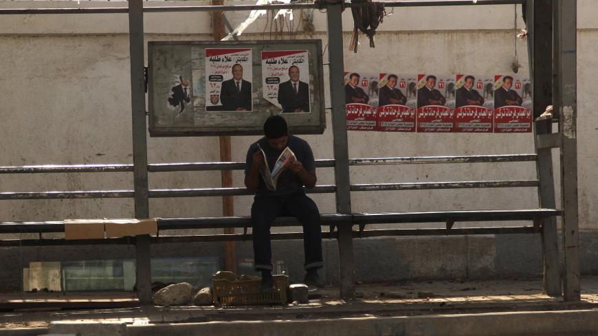 A man reads a newspaper at a bus stop in front of electoral posters in Alexandria, Egypt, October 18, 2015. Egyptians turned out in low numbers on Sunday to vote in the first phase of an election hailed by President Abdel Fattah al-Sisi as a milestone on the road to democracy but shunned by critics who say the new chamber will rubber stamp his decisions. REUTERS/Asmaa Waguih - GF10000249681