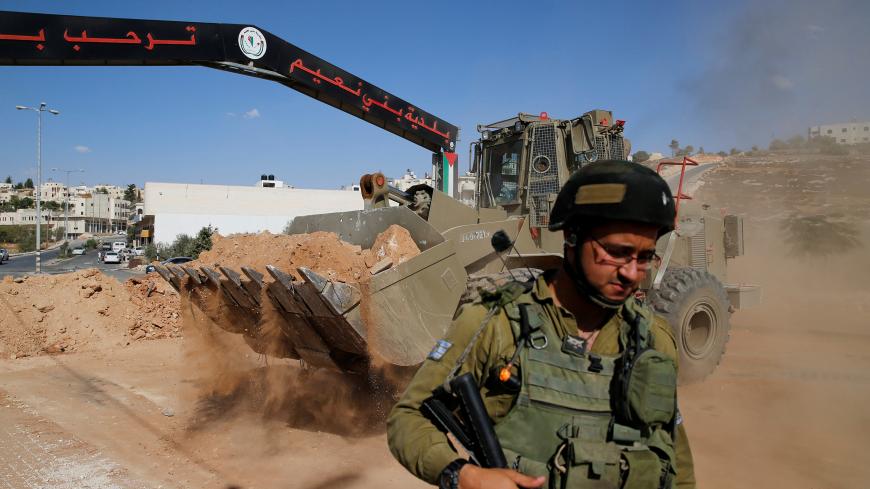 An Israeli soldier stands guard as an Israeli military bulldozer opens the entrance of the West Bank village of Bani Na'im, near Hebron September 21, 2016. REUTERS/Ammar Awad - S1BEUCPBUNAA