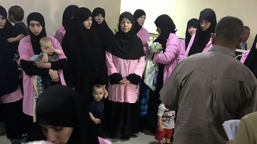 TOPSHOT - A picture taken on April 29, 2018 in the Iraqi capital Baghdad's Central Criminal Court shows Russian women who have been sentenced to life in prison on grounds of joining the Islamic State (IS) group standing with children in a hallway. - Iraq sentenced 19 Russian women to life in prison for joining IS group on April 29, according to an AFP journalist and a judicial source. 
The president of Baghdad's Central Criminal Court, which deals with terrorism cases, said the women were found guilty of "j