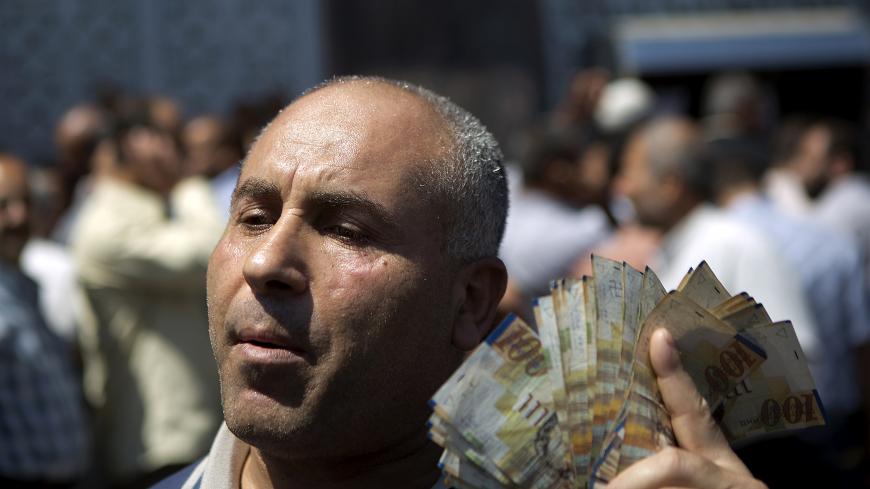 A civil servant paid by the Palestinian Authority displays New Israeli Shekels (NIS) bills after he took his salary from a bank in Gaza City on June 11, 2014. Gaza's banks reopened today after being closed for six days by Hamas forces in a row over pay which was the first hitch in a reconciliation deal between Hamas and the Palestine Liberation Organisation that began with the formation of a new unity government. The PA has so far refused to pay Hamas's 50,000 civil servants, who are not registered as its e