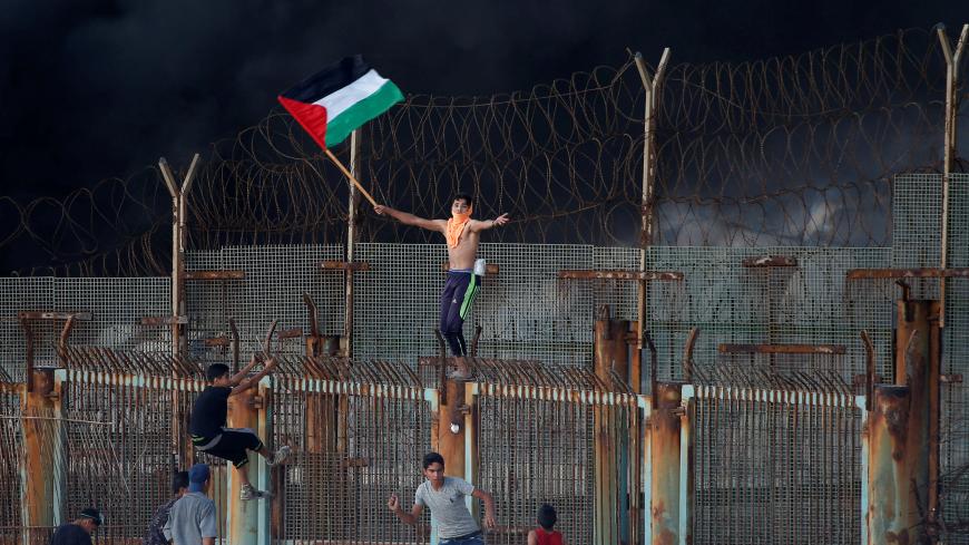 A demonstrator holding a Palestinian flag gestures as he climbs over the Israeli fence during a protest calling for lifting the Israeli blockade on Gaza, at the maritime border with Israel, in the northern Gaza Strip October 8, 2018. REUTERS/Mohammed Salem - RC18961E5F10