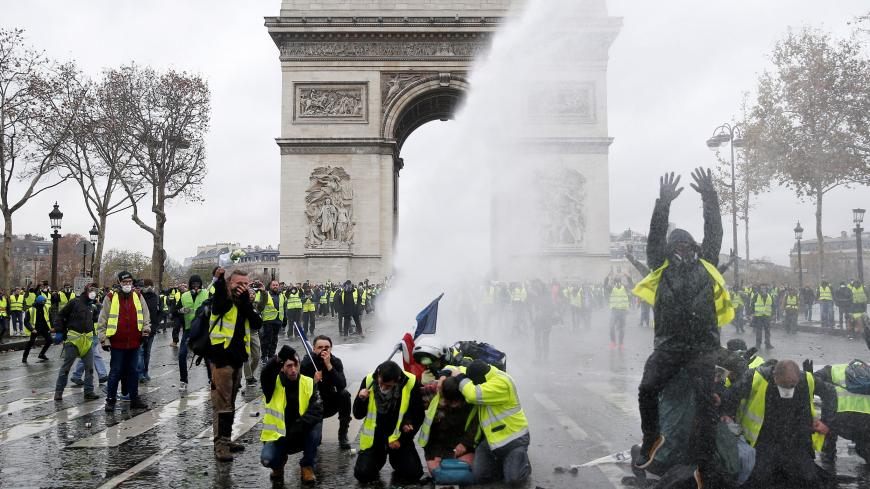 Protesters wearing yellow vests, a symbol of a French drivers' protest against higher diesel taxes, stand up in front of a police water canon at the Place de l'Etoile near the Arc de Triomphe in Paris, France, December 1, 2018. REUTERS/Stephane Mahe - RC117F7CB820