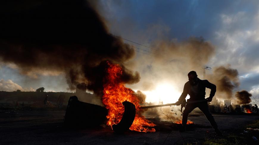 A Palestinian moves a burning tire during clashes with Israeli troops near the Jewish settlement of Beit El, near Ramallah, in the Israeli-occupied West Bank December 13, 2018. REUTERS/Mohamad Torokman - RC110351F370