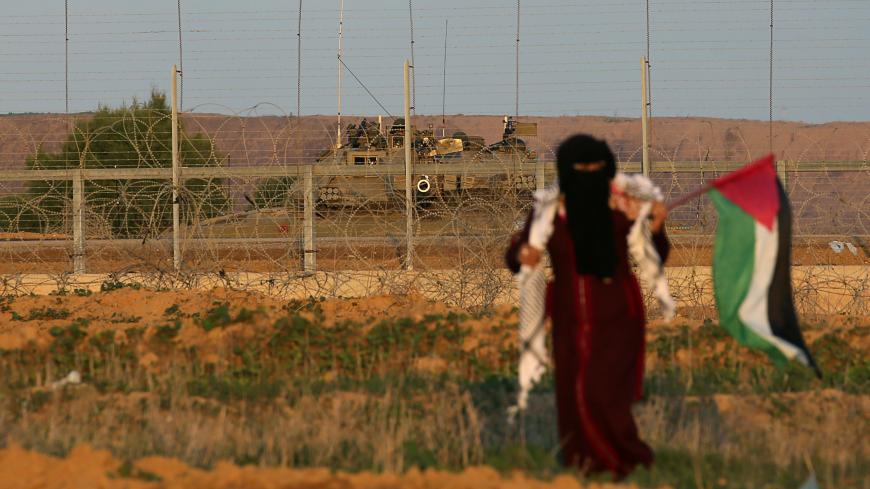 Israeli soldiers are seen on their military vehicle as a Palestinian woman walks during a protest at the Israel-Gaza border fence, in the southern Gaza Strip December 21, 2018. REUTERS/Ibraheem Abu Mustafa - RC1831F545E0
