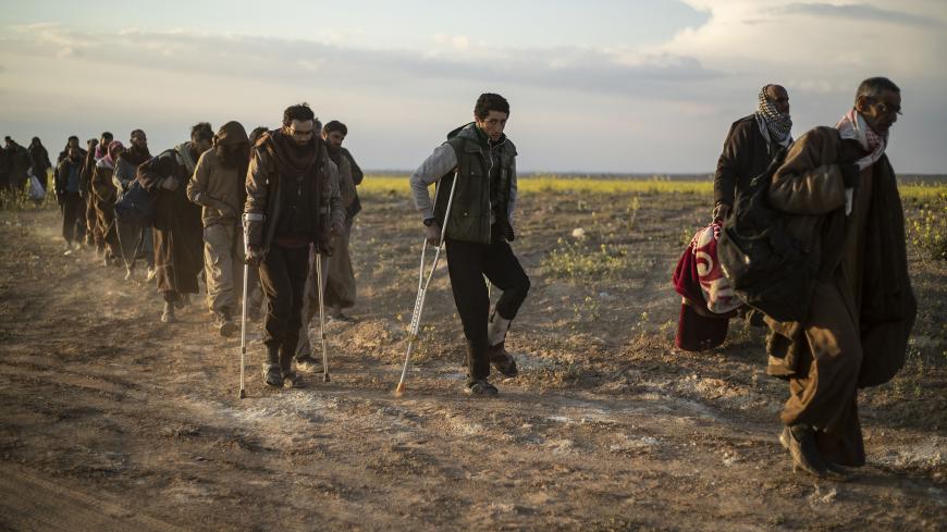 Men suspected of being Islamic State (IS) group fighters walk together towards a screening point for new arrivals run by US-backed Syrian Democratic Forces, where suspected jihadists -- many of them wounded -- were being interrogated outside Baghouz in the eastern Syrian Deir Ezzor province on March 6, 2019. - Veiled women carrying babies and wounded men on crutches hobbled out of the last jihadist village in eastern Syria on March 6 after US-backed forces pummelled the besieged enclave. The Syrian Democrat