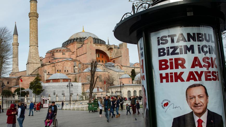 People walk past an election poster bearing the picture of Turkish President Recep Tayyip Erdogan, and reading "Istanbul is a love story for us", in front of the Hagia Sophia museum in Istanbul, on March 26, 2019, ahead of March 31 local elections. - Turkish President on March 24 mooted the possibility of renaming Istanbul's Hagia Sofia museum as a mosque, in comments during a television interview. The museum, a UNESCO World Heritage site, receives millions of visitors every year. (Photo by Yasin AKGUL / AF