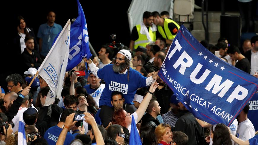 A supporter of Israeli Prime Minister Benjamin Netanyahu's Likud party waves flags, one bearing the name of U.S. President Donald Trump, as the crowd reacts to exit polls in Israel's parliamentary election at the party headquarters in Tel Aviv, Israel April 10, 2019. REUTERS/Ronen Zvulun - RC12929E4A50