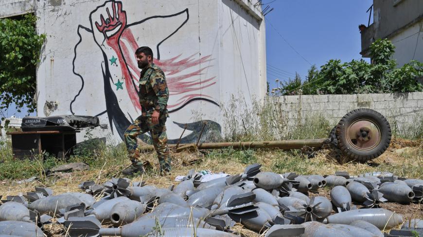A Syrian government soldier walks past strewn mortar shells in the village of Qalaat al-Madiq, some 45 kilometres northwest of the central city of Hama, on May 17, 2019. - Syrian government forces a week prior had recaptured the northwestern town on the southwestern edge of the jihadist-controlled Idlib region, from around which jihadists and allied rebels were launching rockets on their Russian ally's key airbase. The capture of the town of Qalaat al-Madiq comes after weeks of intensified air strikes and s