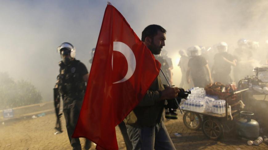 A protester holds a Turkish flag as riot police order them to evacuate Gezi Park in central Istanbul June 15, 2013. Thousands of people took to the streets of Istanbul overnight on Sunday, erecting barricades and starting bonfires, after riot police firing teargas and water cannon stormed a park at the centre of two weeks of anti-government unrest. Lines of police backed by armoured vehicles sealed off Taksim Square in the centre of the city as officers raided the adjoining Gezi Park late on Saturday, where
