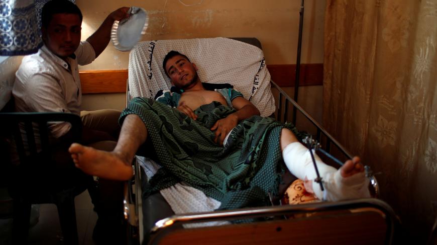 A man cools off an injured Palestinian as he lies on a bed at a hospital in Gaza City May 15, 2018. REUTERS/Mohammed Salem - RC1240F48280