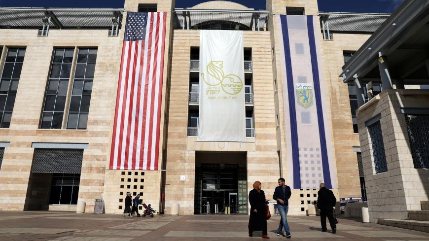 People walk at the Jerusalem's city hall as the American and Israeli national flags hang on the municipality building in Jerusalem December 7, 2017. REUTERS/Ammar Awad - RC121A0E97D0