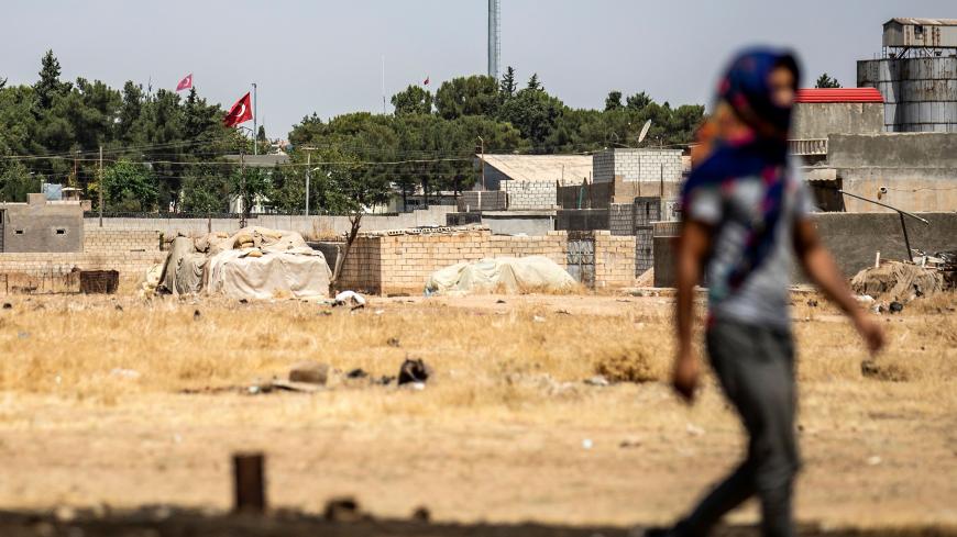 A Syrian Kurd walks during a protest and sit-in against Turkey, in the town of Ras al-Ain in Syria's Hasakeh province near the Turkish border on August 9, 2019, with the flags of Turkey seen across the border in the background. (Photo by Delil SOULEIMAN / AFP)        (Photo credit should read DELIL SOULEIMAN/AFP/Getty Images)