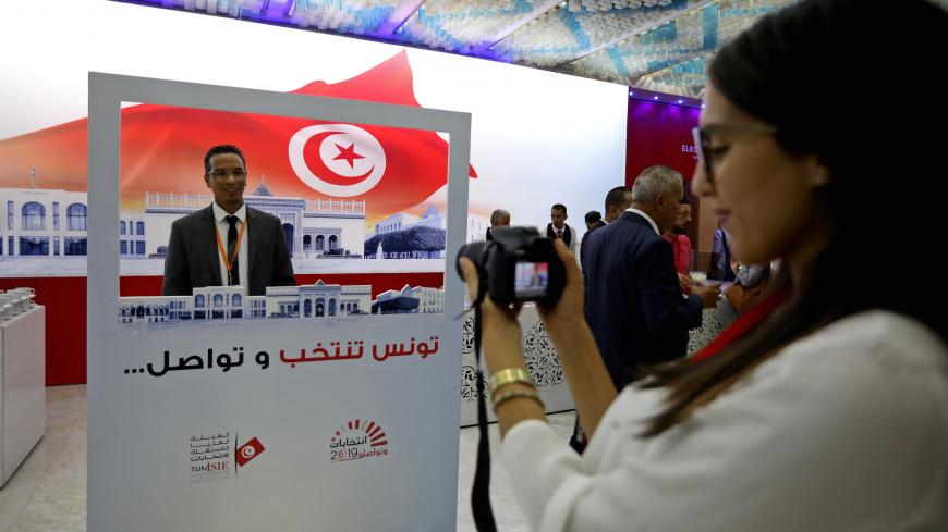 A man poses for a picture with a poster that reads in Arabic "Tunis, Elect and Continue" during the opening of the media center for the presidential election in Tunis, Tunisia, September 12, 2019. REUTERS/Muhammad Hamed - RC1110D7B900