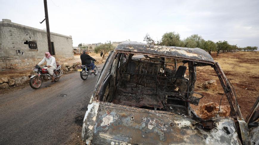 A picture taken on October 28, 2019 shows Syrian bikers riding past a damaged car at the site of a suspected US-led operation against Islamic State (IS) chief Abu Bakr al-Baghdadi the previous day, on the edge of the small Syrian village of Barisha in the country's opposition-held northwestern Idlib province. - US President Donald Trump announced that Baghdadi, the elusive leader of the jihadist group and the world's most wanted man, was killed in the early hours of Octobe 27 in an overnight US raid near th