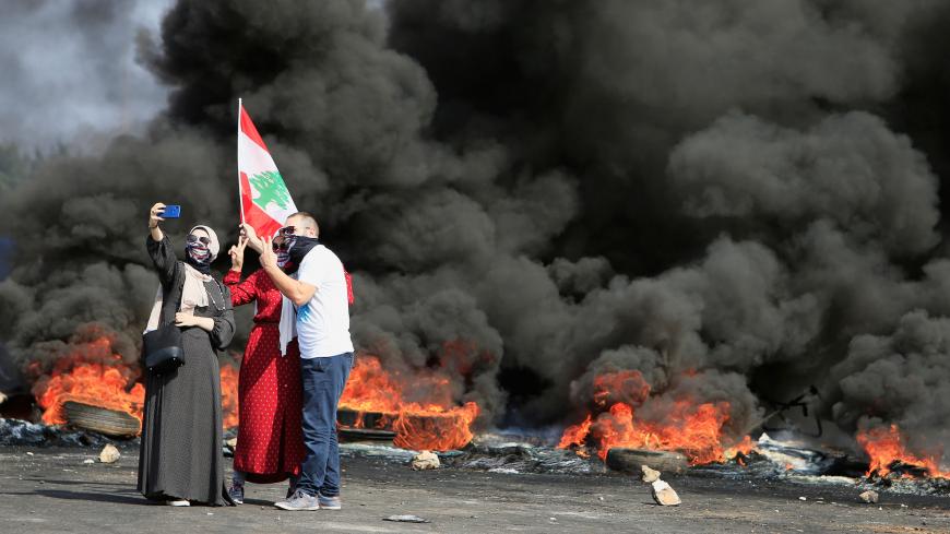 Demonstrators take a selfie in front of burning tires during a protest targeting the government over an economic crisis, at Barja area blocking off a main road leading from southern Lebanon to Beirut, October 18, 2019. REUTERS/Ali Hashisho - RC1FB9E67800