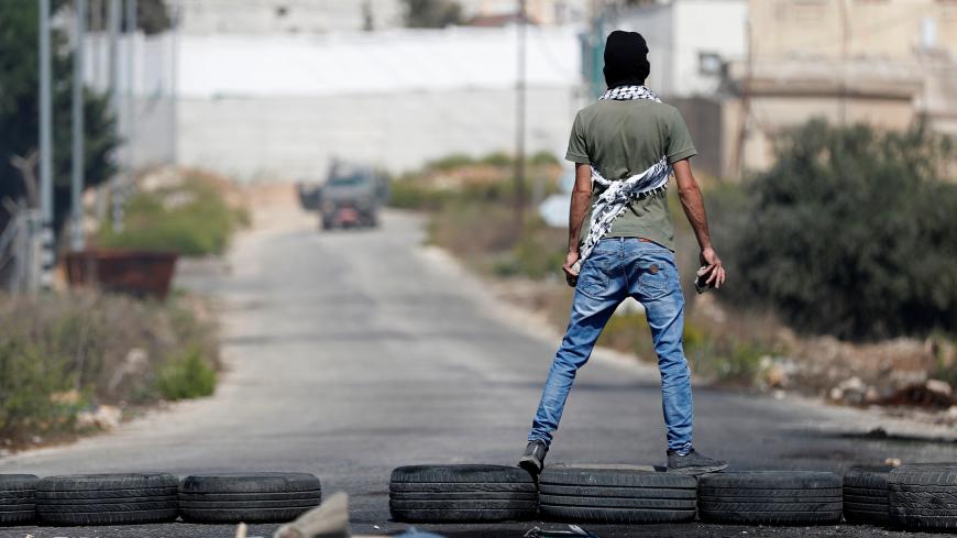 A demonstrator stands on tires in front of Israeli forces during a protest to show solidarity with Palestinian prisoners held in Israeli jails, near the Jewish settlement of Beit El in the Israeli-occupied West Bank October 1, 2019. REUTERS/Mohamad Torokman - RC1E64FD2C50