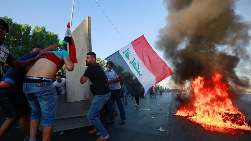Demonstrators hold the Iraqi flag near burning objects at a protest during a curfew, three days after the nationwide anti-government protests turned violent, in Baghdad, Iraq October 4, 2019. REUTERS/Alaa al-Marjani - RC1CCAB95C40
