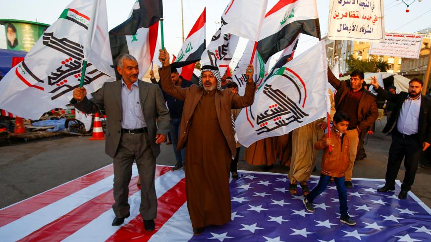 Iraqi people walk on a U.S. flag in a protest after an airstrike at the headquarters of Kataib Hezbollah militia group in Qaim, in the holy city of Najaf, Iraq December 30, 2019. REUTERS/Alaa al-Marjani - RC2Q5E9X7DV4